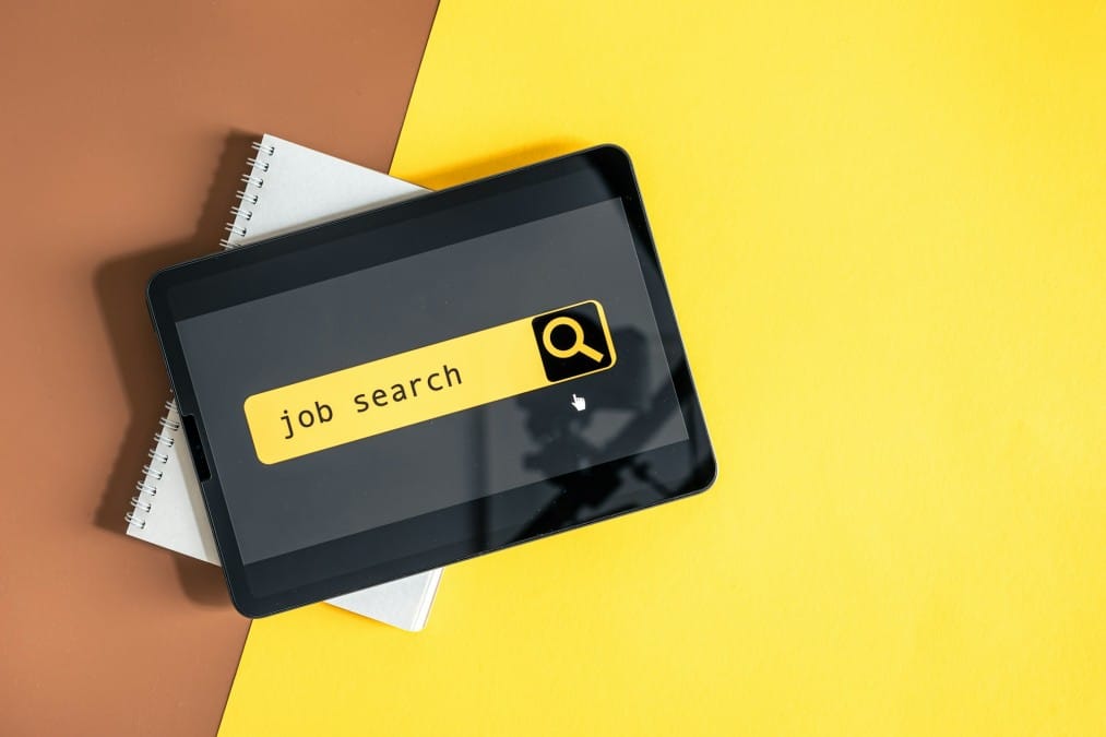 Top view of digital tablet with search job on screen on a yellow background.